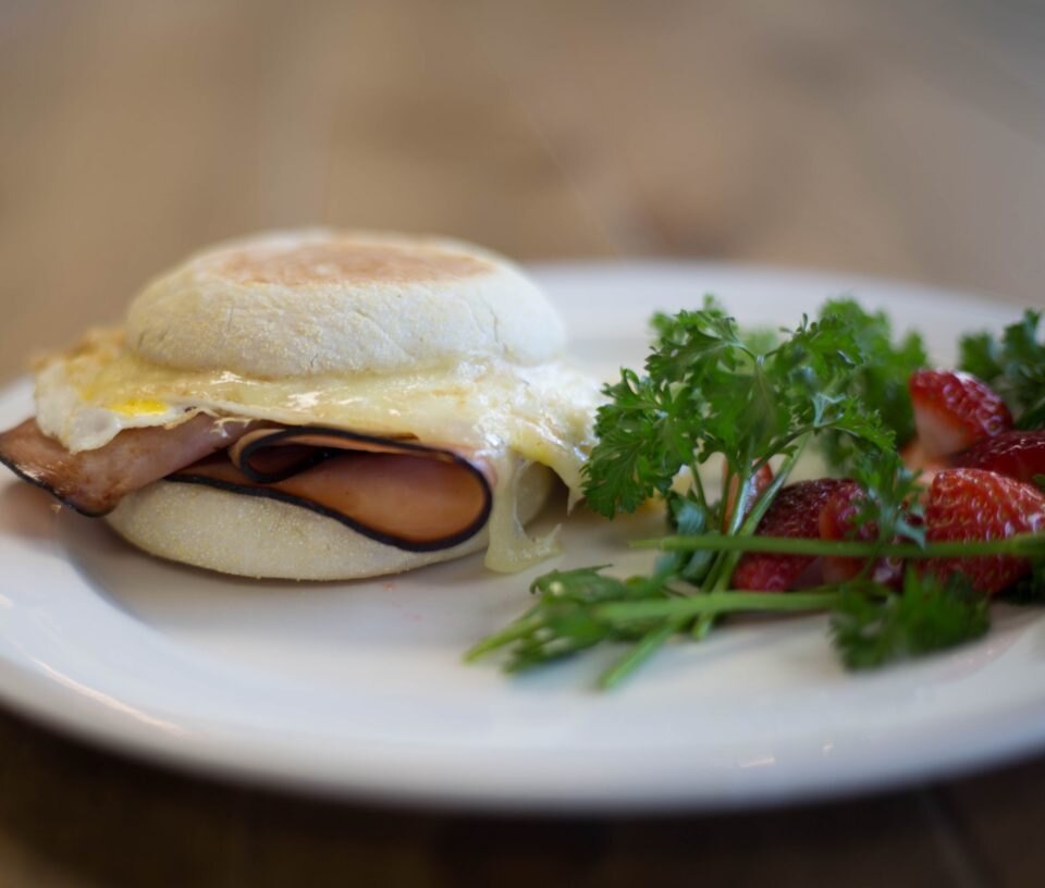 English muffin with ham, egg and melted cheese beside parsley and strawberries