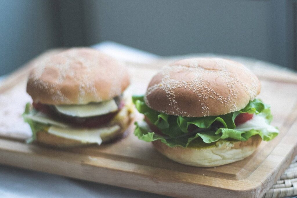 Two burgers with lettuce and cheese on a wooden cutting board
