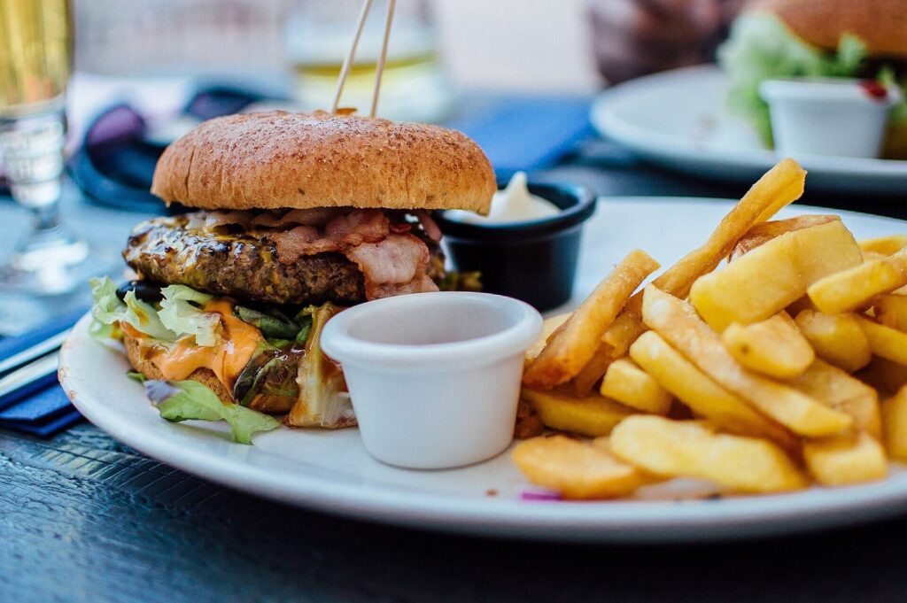 Bacon burger with chunky fries and a dip cup on a white plate