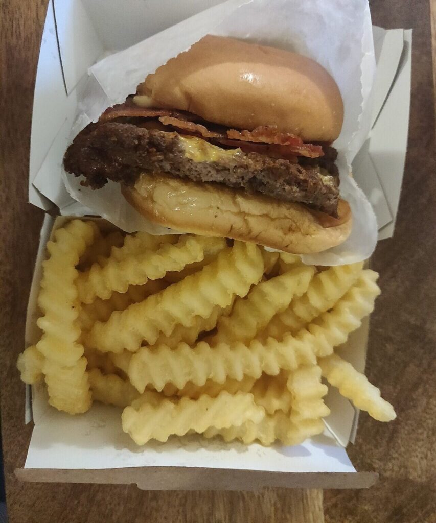 Bacon cheeseburger with crinkle-cut fries in a plain paper tray