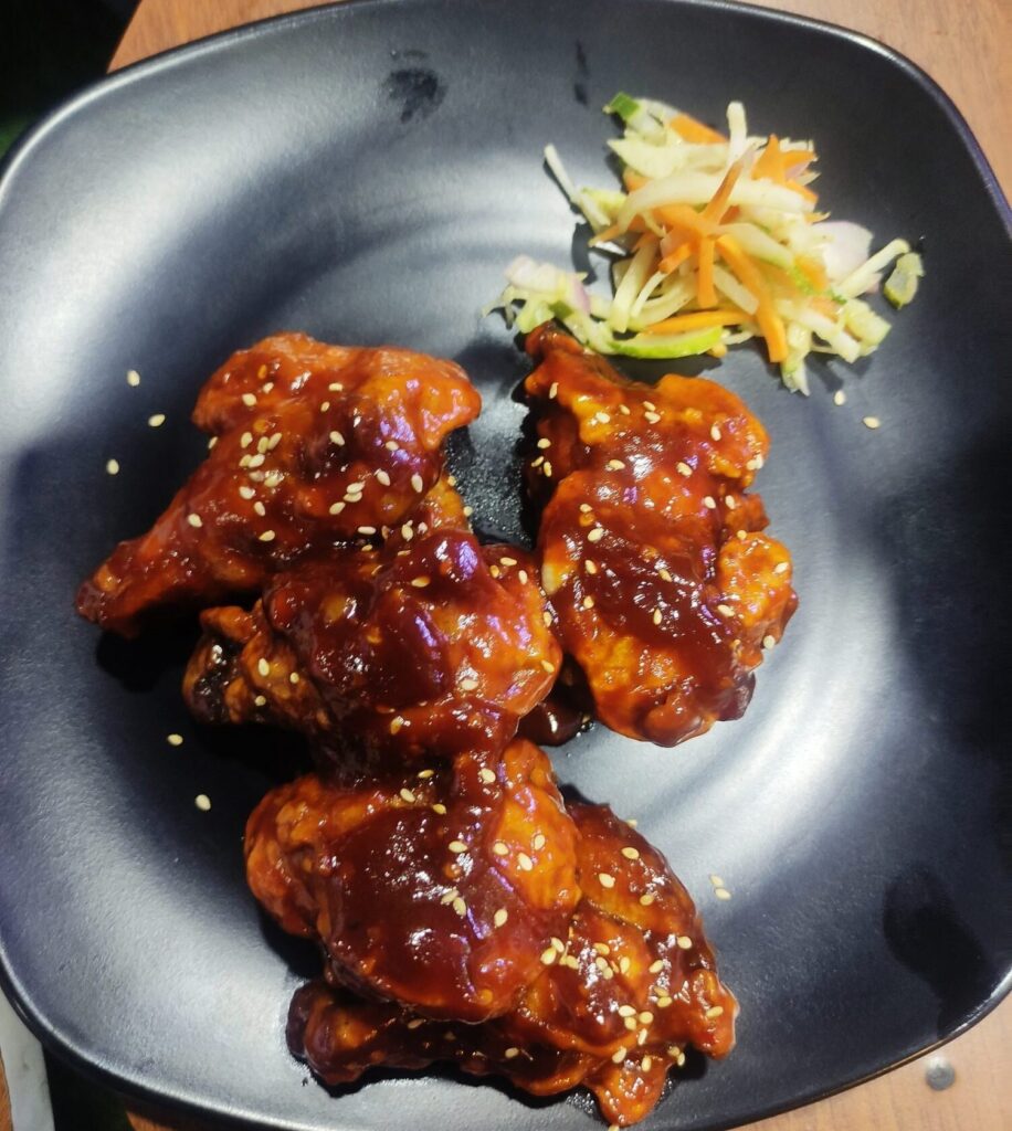 Sticky glazed wings with sesame and a small slaw on a dark plate