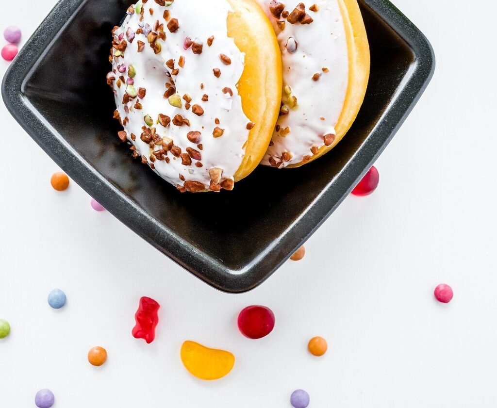 White-glazed doughnuts with nuts in a dark dish, sweets scattered around