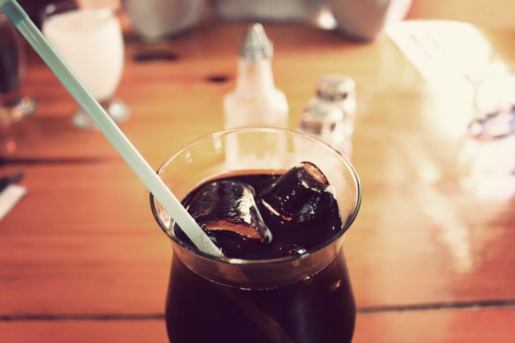 Glass of cola with ice and a straw on a wooden table