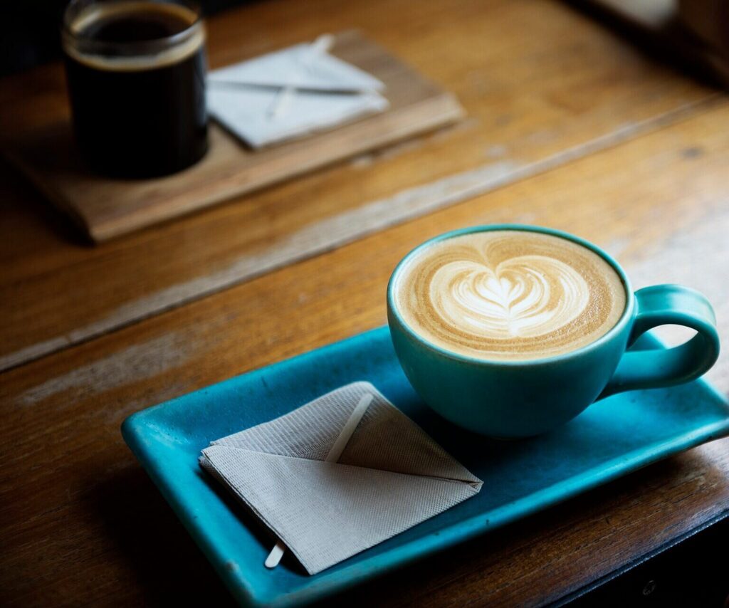 Latte with leaf art in a teal cup on a tray, black coffee behind