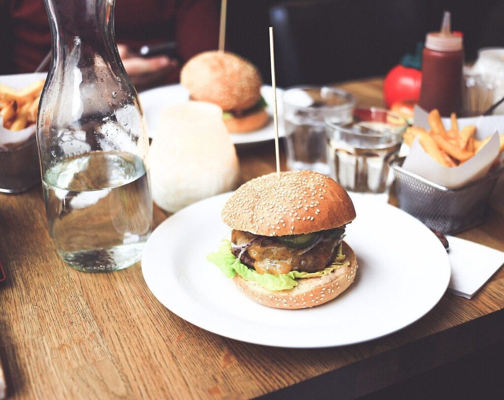 Sesame cheeseburger on a plate with fries baskets, water and a second burger behind
