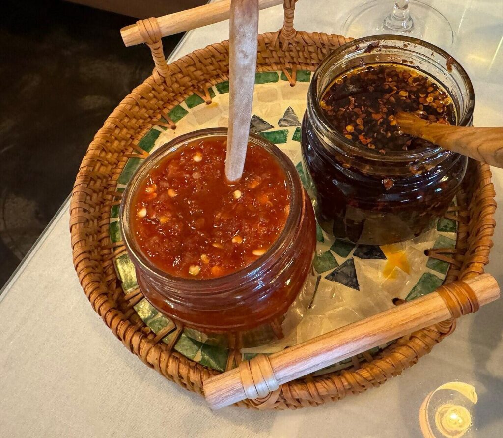 Two jars of chilli sauce and chilli oil with wooden spoons in a basket