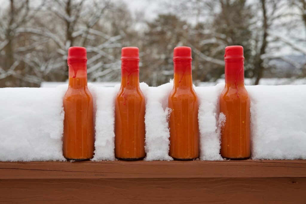 Four unlabelled bottles of homemade hot sauce in the snow