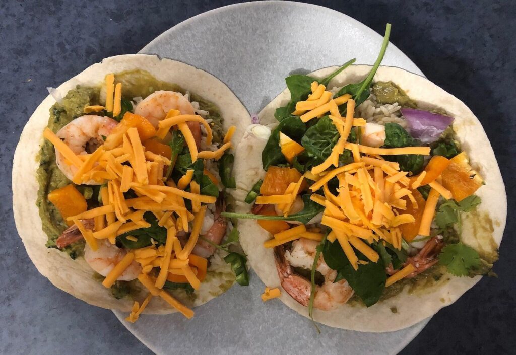 Two shrimp tacos with cheddar, spinach and peppers on a grey plate